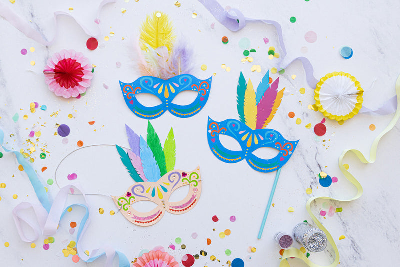Colorful carnival masks and crafting supplies laid out on a white table for a DIY mask activity