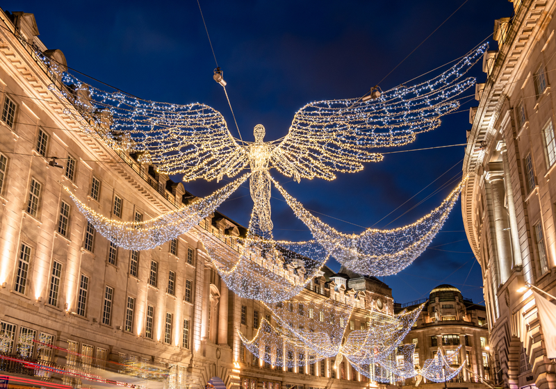 Nighttime London street lit by Christmas lights with a large illuminated angel spanning between buildings