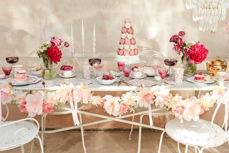 Pastel wedding dessert table with pink macarons centerpiece, teacups, floral garlands and candles.