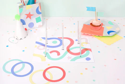 Colorful hoopla party game setup with a game board pegs rings confetti a cupcake and a gift bag