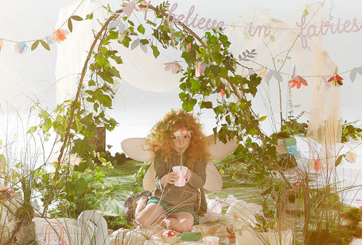 Fairy with wings sits under a leafy floral arch in a bright craft scene.