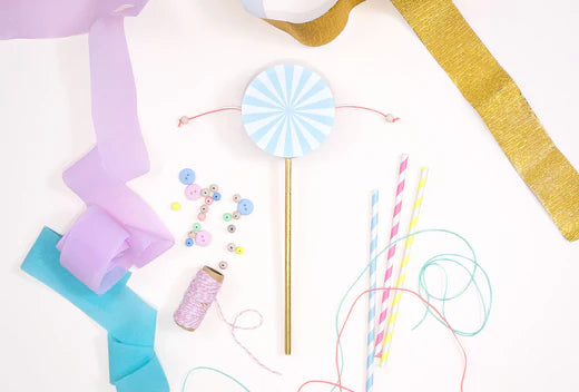 Craft supplies for a summer party including ribbons, buttons, thread, and a blue striped pinwheel on a white background.