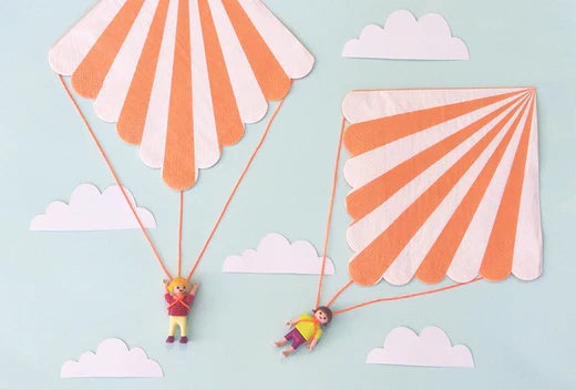 Two striped paper kites with toy figures suspended from strings against a pale blue sky with clouds