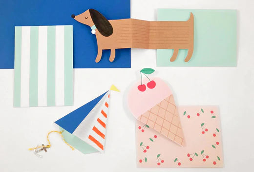 Colorful collage of paper notecards and craft shapes including a dachshund, sailboat, ice cream cone, and striped cards
