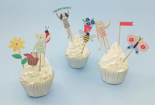 Three cupcakes topped with whimsical paper figures and flags for a picnic style cake.