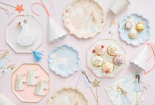 Pastel princess party spread with cookies, cupcakes, and decorative plates on a pale pink table.