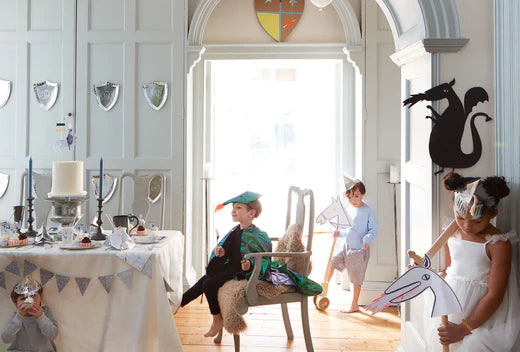 Children in knight and princess costumes explore a bright room set as a magical castle with a dragon silhouette