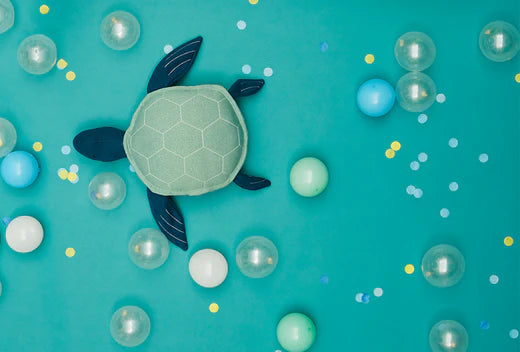 Teal background with a soft turtle plush surrounded by bubbles and confetti.