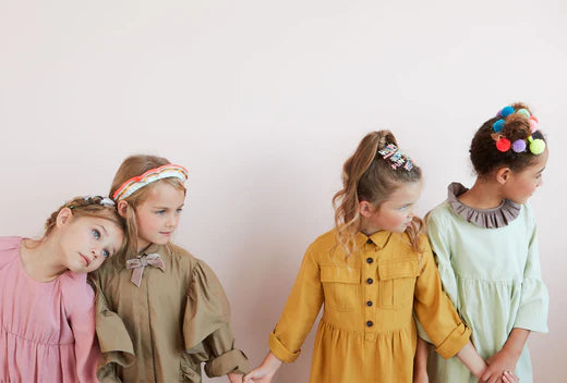 Four girls in pastel dresses pose together for a friendship bracelet craft article