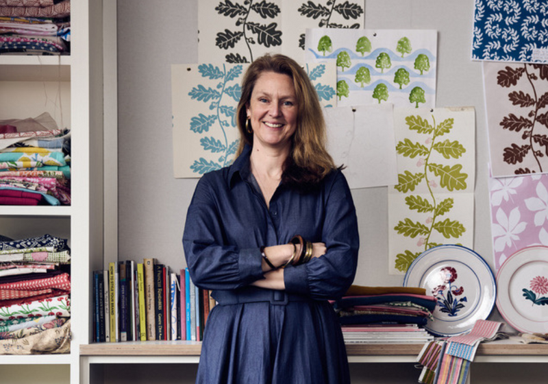 Portrait of textile designer Molly Mahon in her studio with botanical prints on the wall and fabric swatches.
