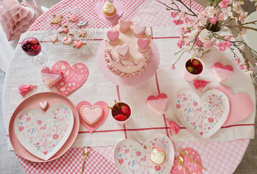 Valentine themed dessert table with pink cake heart cookies and floral accents on a pink gingham tablecloth.