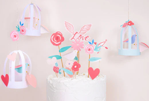 Valentine crafts display with hanging paper lanterns, pink flowers and a Love themed cake centerpiece.