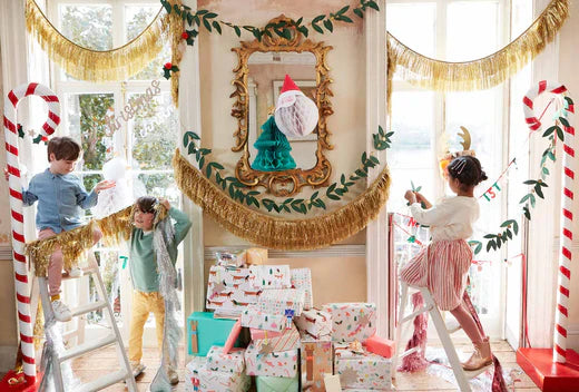 Children creating festive paper chains in a bright room with gold tassel garlands and candy cane decor