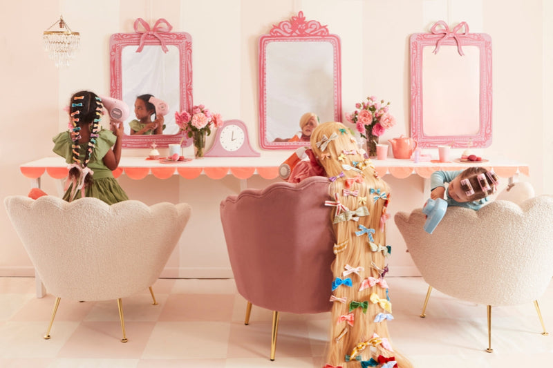 Children in pastel pink salon chairs get cute school hairstyles with ribbons and rollers.
