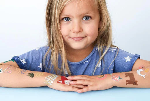 Young girl with colorful temporary tattoos on her arms resting on a light blue surface.