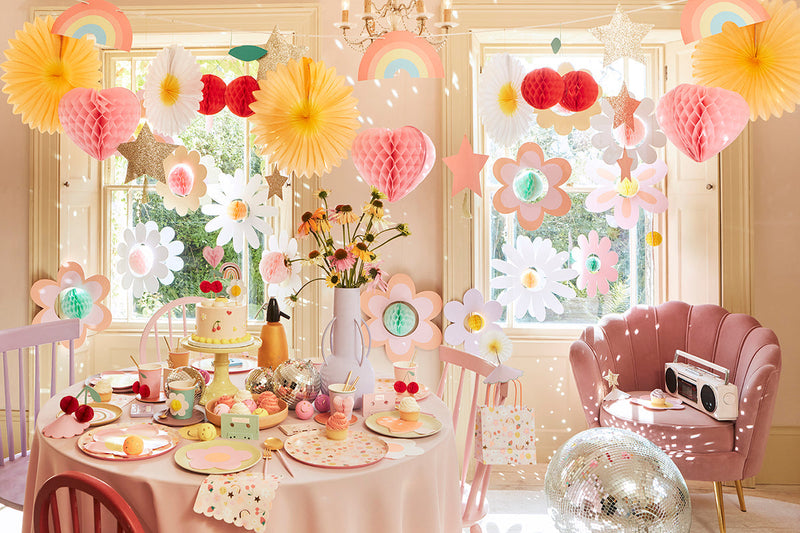 Bright pastel tween party room with paper flowers rainbows and a decorated dessert table.