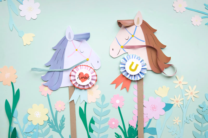 Two pastel paper hobby horses with decorative rosettes on a light mint backdrop.