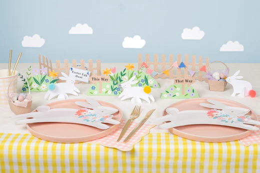A yellow and white striped table is decorated with pink and leaping bunny plates. Cardboard floral and bunny decorations are placed in the centre.