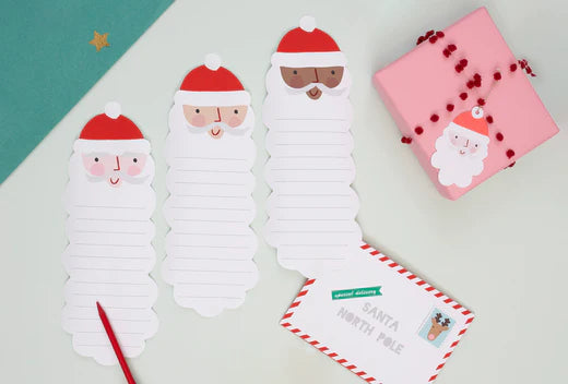 3 lined pages in the shape of Santas are placed on a light green background, with a pink package and Santa gift tag besides them.