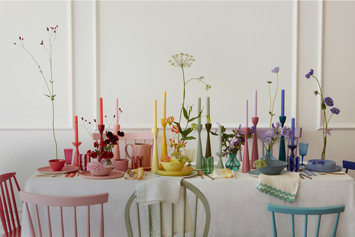 An array of rainbow tableware, including tall candles, scalloped napkins, and plates, sitting on a dining table