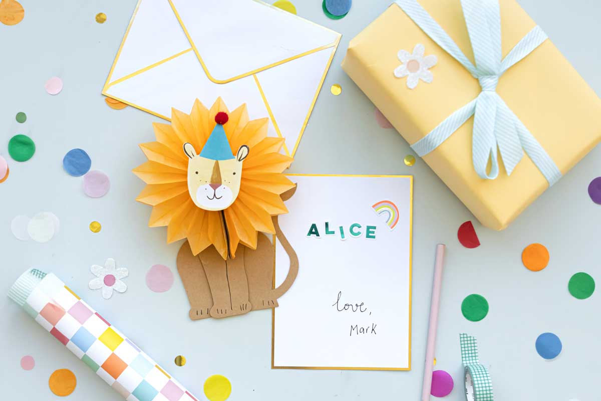 A honeycomb lion card placed next to a blank letter that has been written on amid rainbow confetti.