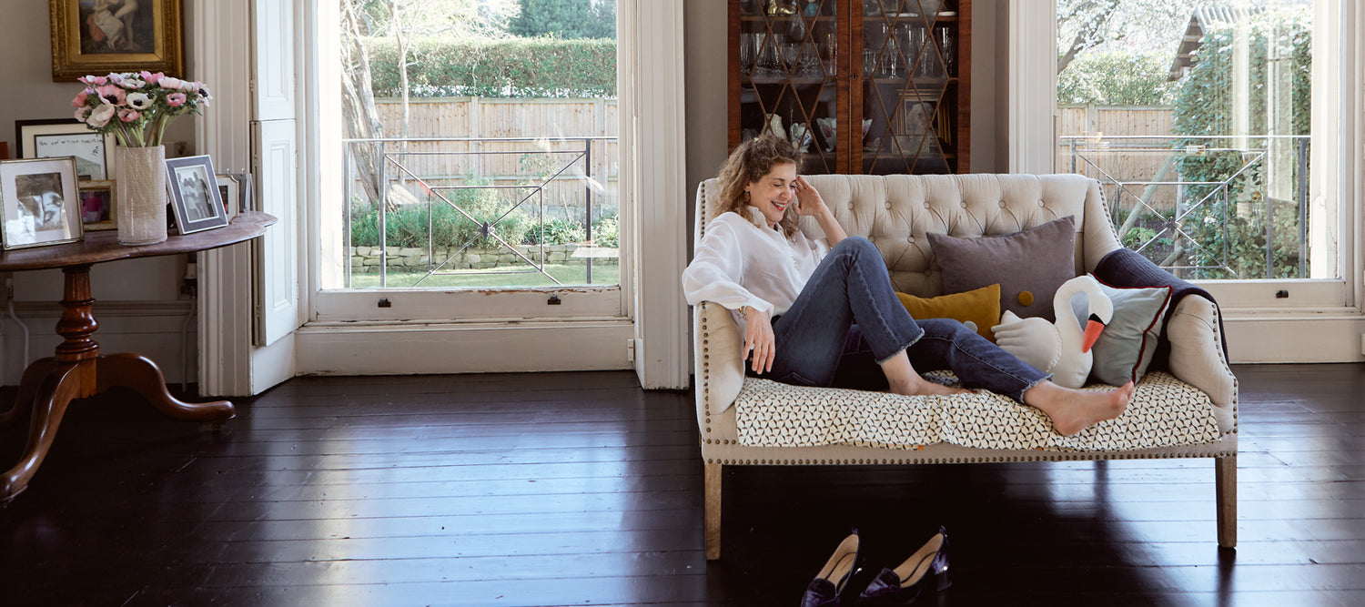 Meredithe Stuart-Smith, founder of Meri Meri, reclines whilst smiling on a sofa in a room accessorized with dark wood.