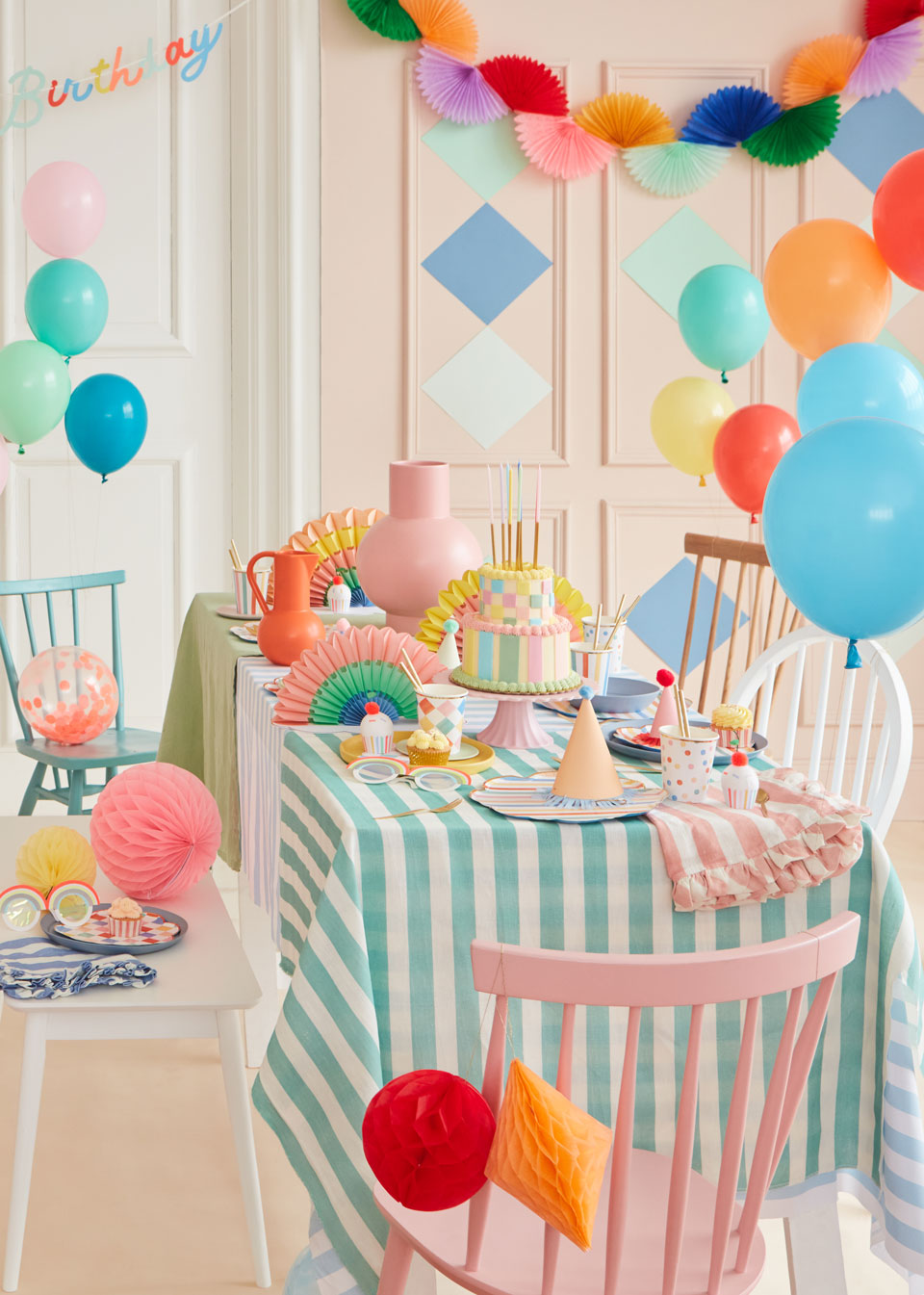 A dining room displays a multitude of colorful garlands and tableware, including honeycomb ornaments, pastel balloons, and ruffled-edge napkins.