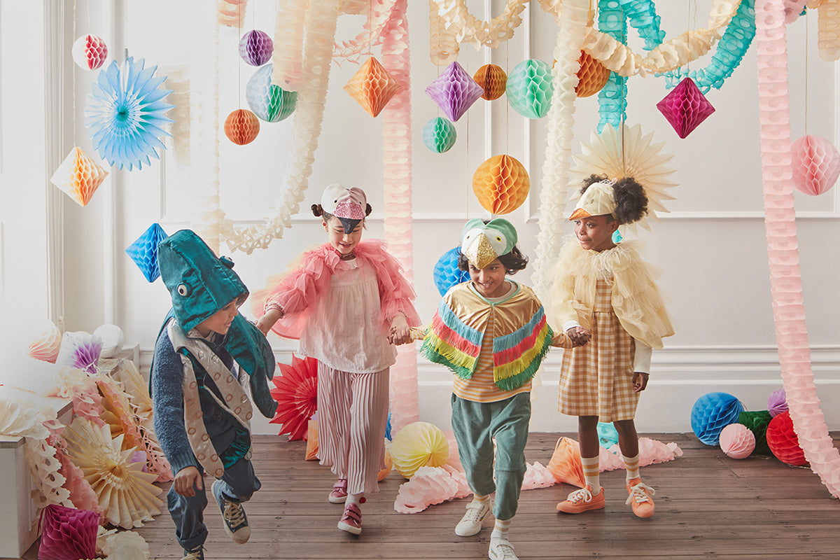 4 children dressed in various animal costumes, including a flamingo and octopus, standing in a room filled with pastel honeycomb hanging decorations and garlands