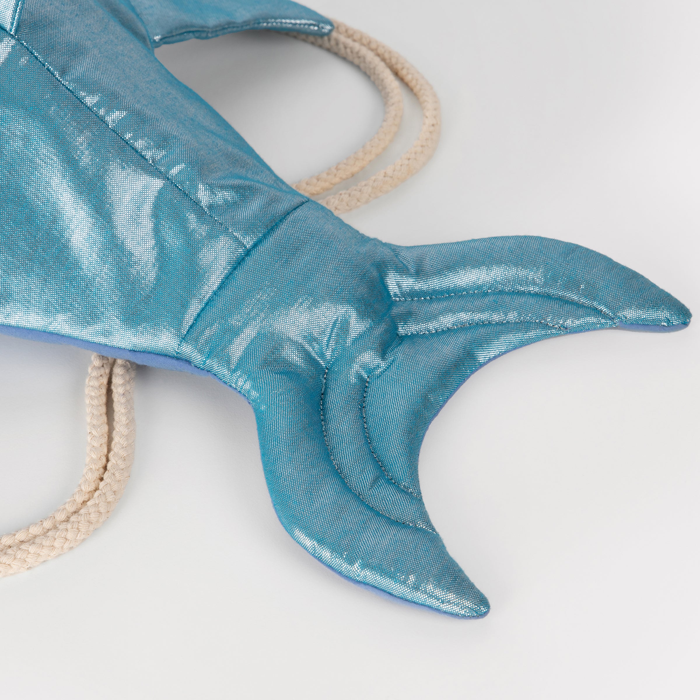 This shiny shark is  a backpack crafted from blue lamé fabric with a cotton lining and cord straps.